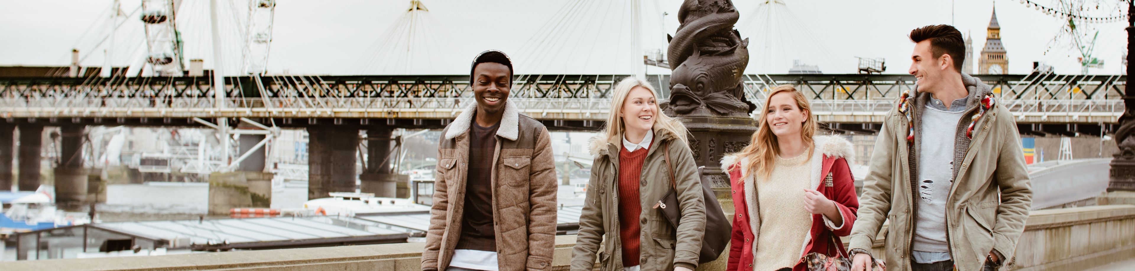 Vier vrienden wandelen langs de Thames in London, met de London Eye op de achtergrond