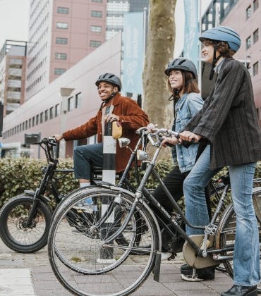 3 jongeren op hun fiets met een fietshelm op wachten voor een stoplicht.