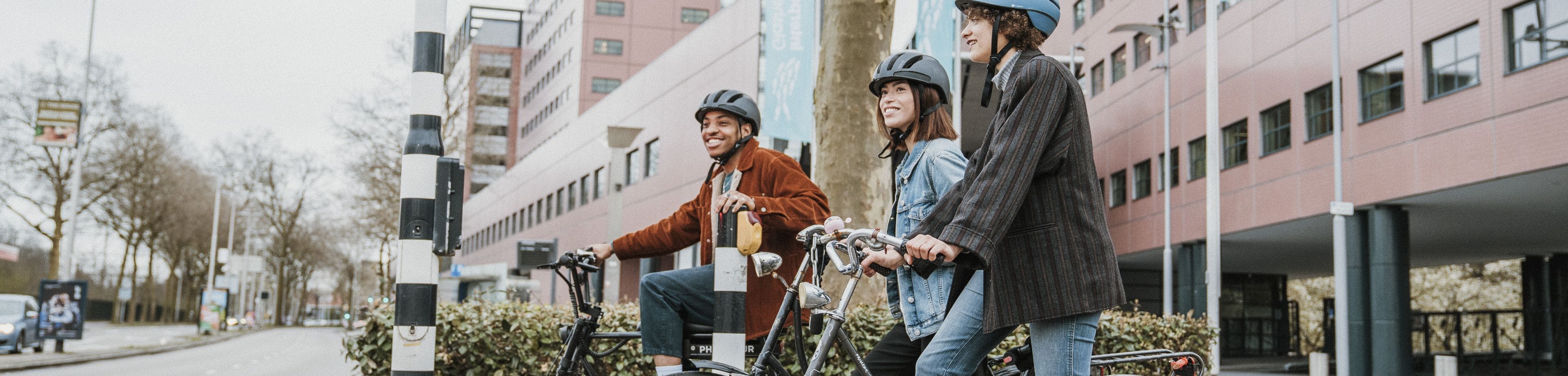 3 jongeren op hun fiets met een fietshelm op wachten voor een stoplicht.