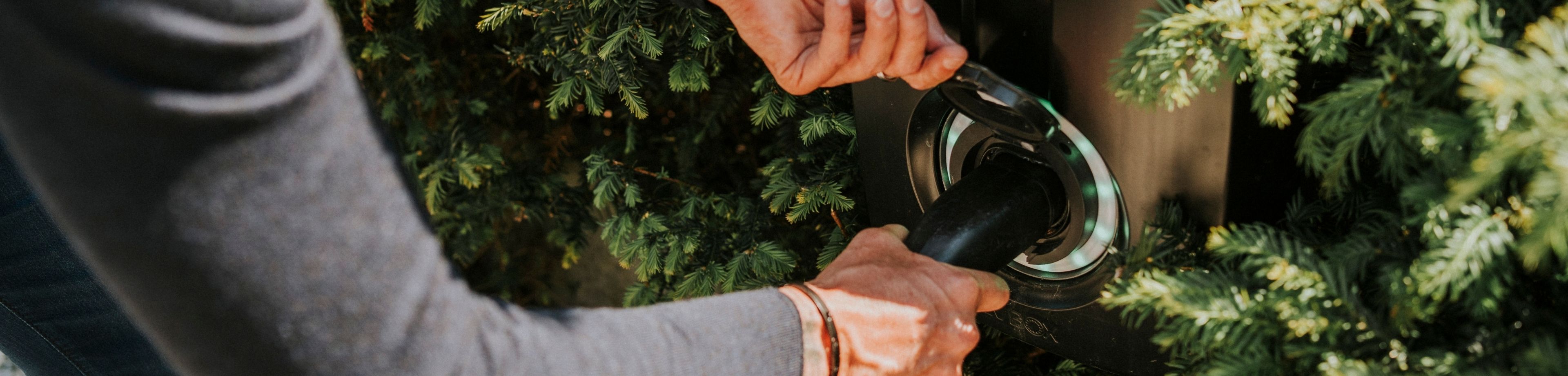 Een persoon steekt de stekker van een elektrische auto in een oplaadpunt. 