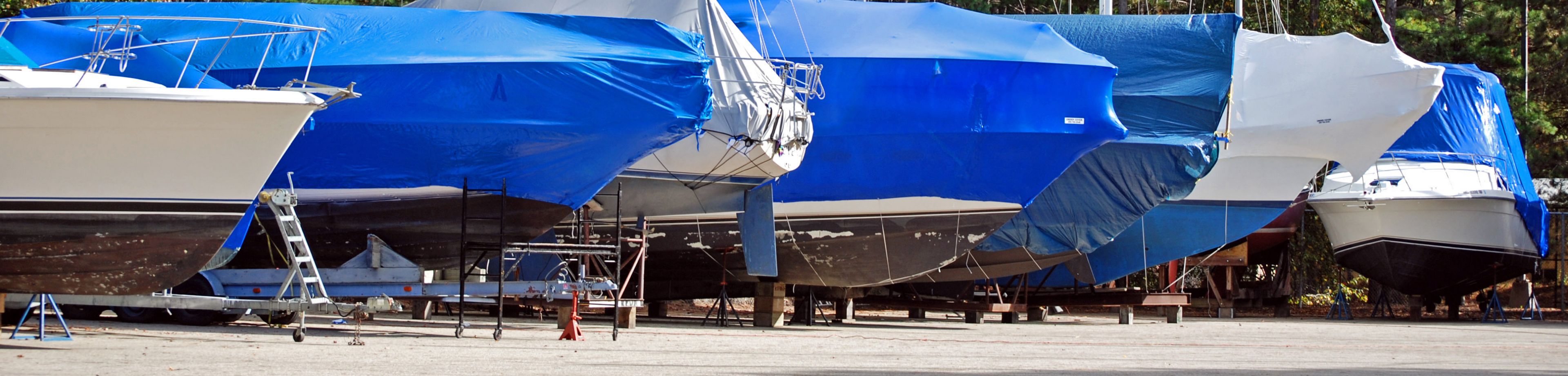 Een rij met boten die op land zijn opgeslagen. Over elke boot is een blauw zeil getrokken.