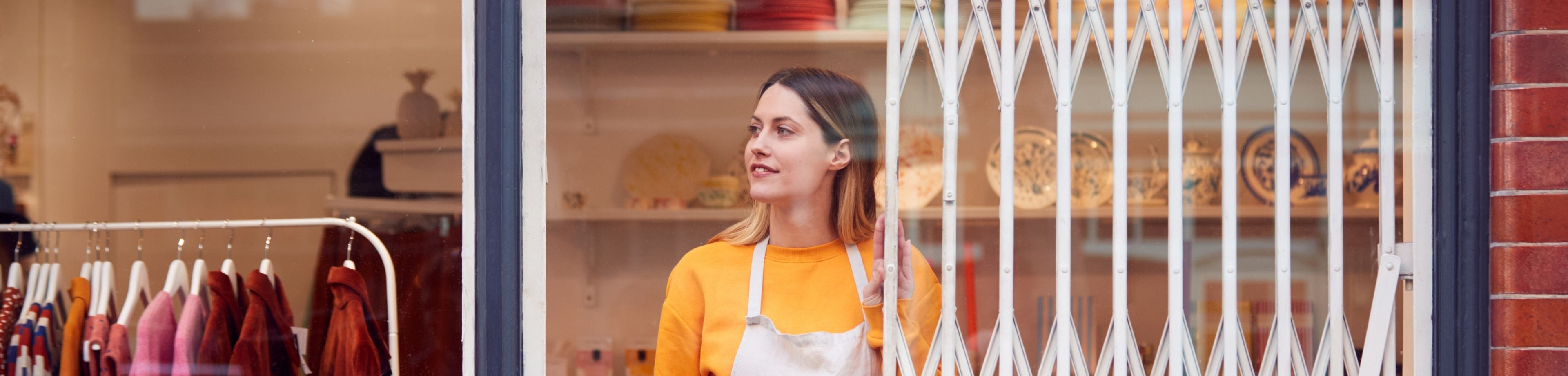 Een winkelmedewerker staat voor de winkel, met het anti-inbraak-hekwerk van de winkel halfgeopend.