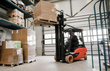 Een heftruck rijdt met een pallet goederen door een magazijn.