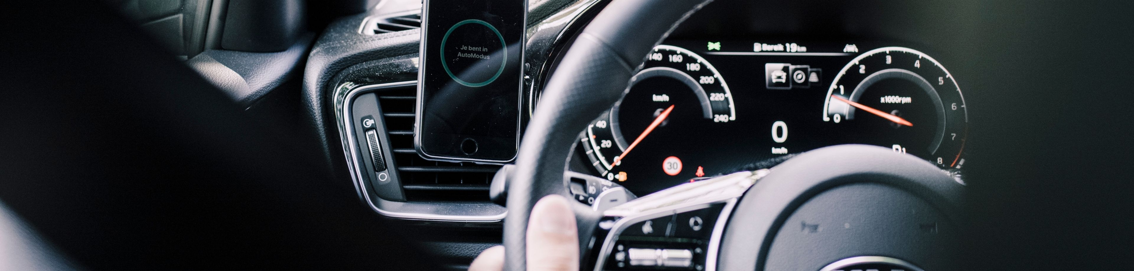 Dashboard van auto met naast het stuur een telefoon in Automodus