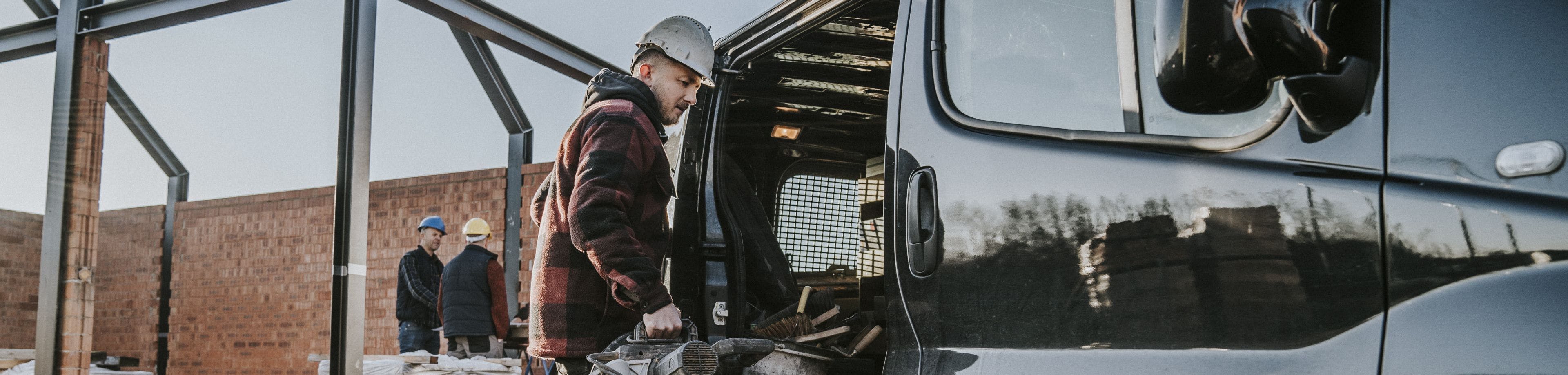Een man met een bouwhelm op zijn hoofd laadt spullen in een bedrijfswagen.