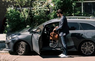 Een man staat naast het geopende portier van zijn auto, en kijkt op het scherm van zijn mobiele telefoon.