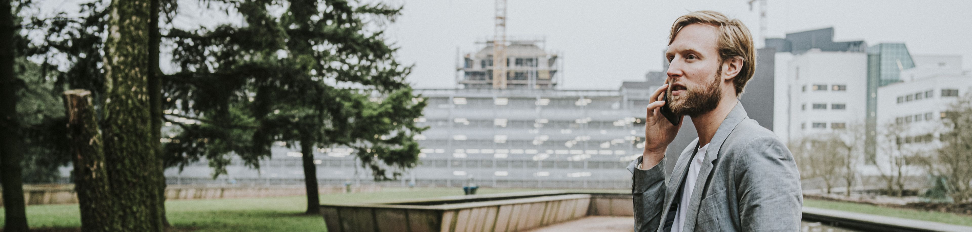 Een man zit te bellen op de rand van een verhoogde vijver in een stadspark.