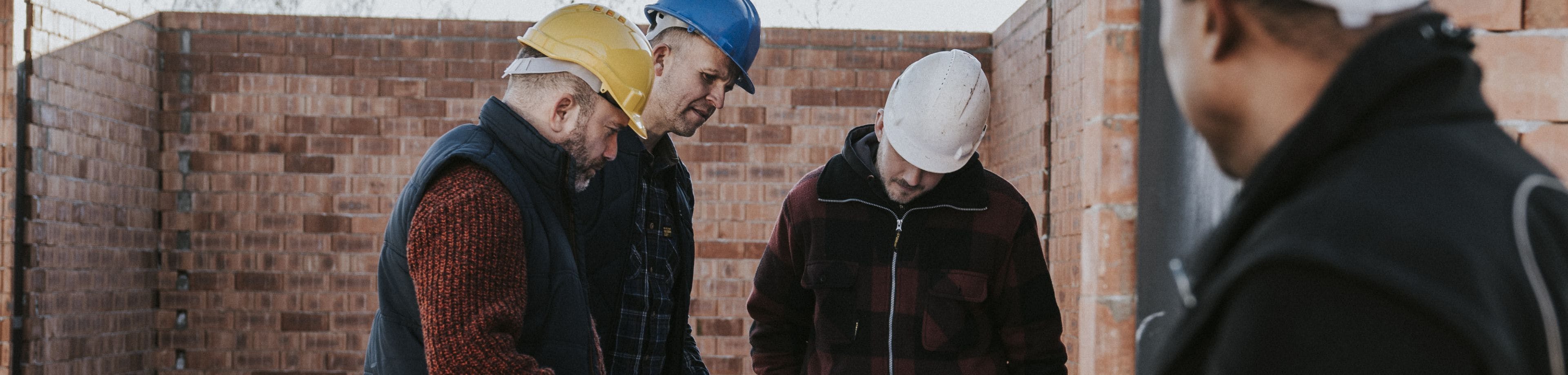 3 mannen staan op een bouwplaats en kijken naar een bouwtekening