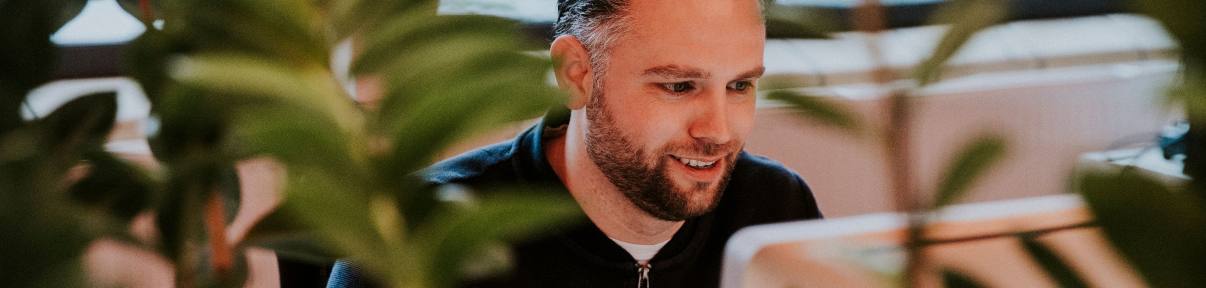 Vriendelijk kijkende man achter laptop met planten op de voorgrond