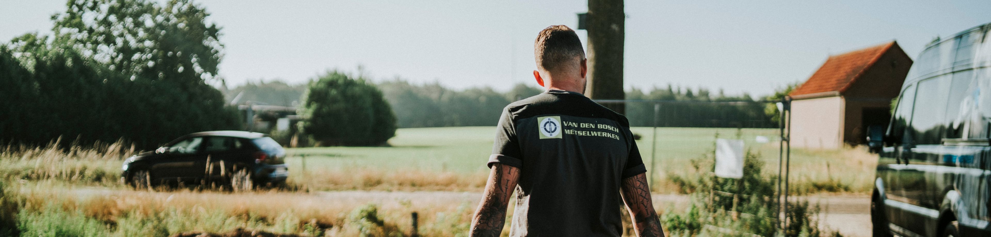 Een man met een shirt van Van Den Bosch metselwerken loopt op een bouwplaats