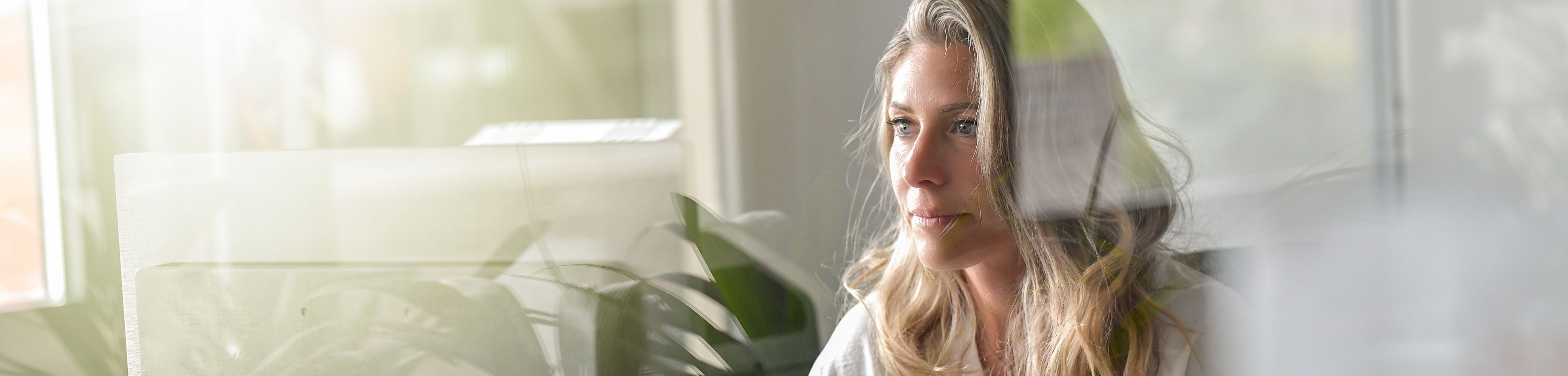 Vrouw met lang blond haar zit achter een beeldscherm en kijkt serieus