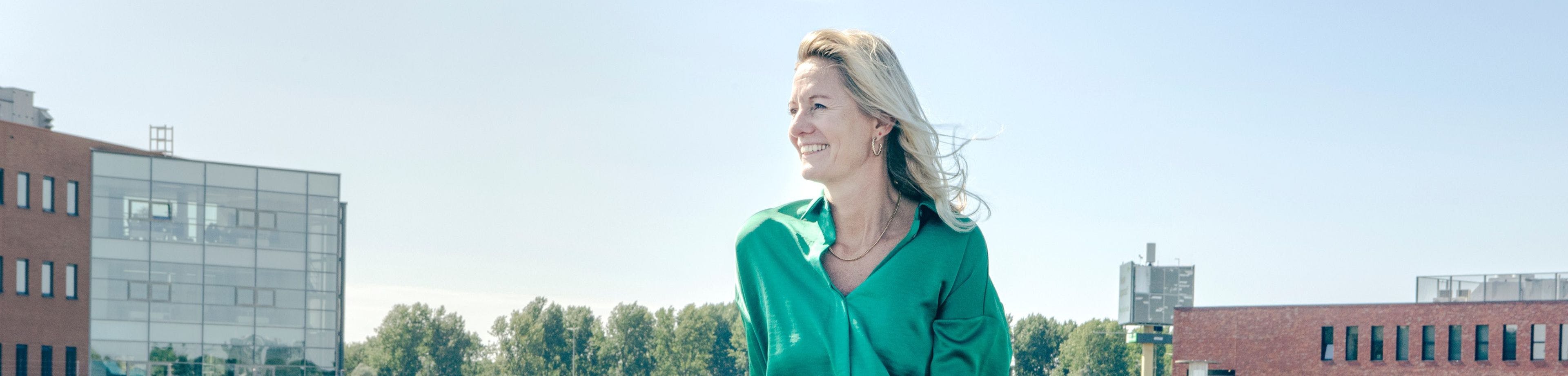 Marjolein Groen, directeur Sustainability en CSR bij mobiliteitsprovider Athlon Nederland, draagt een groene bloes en zit lachend op een parkeerplaats