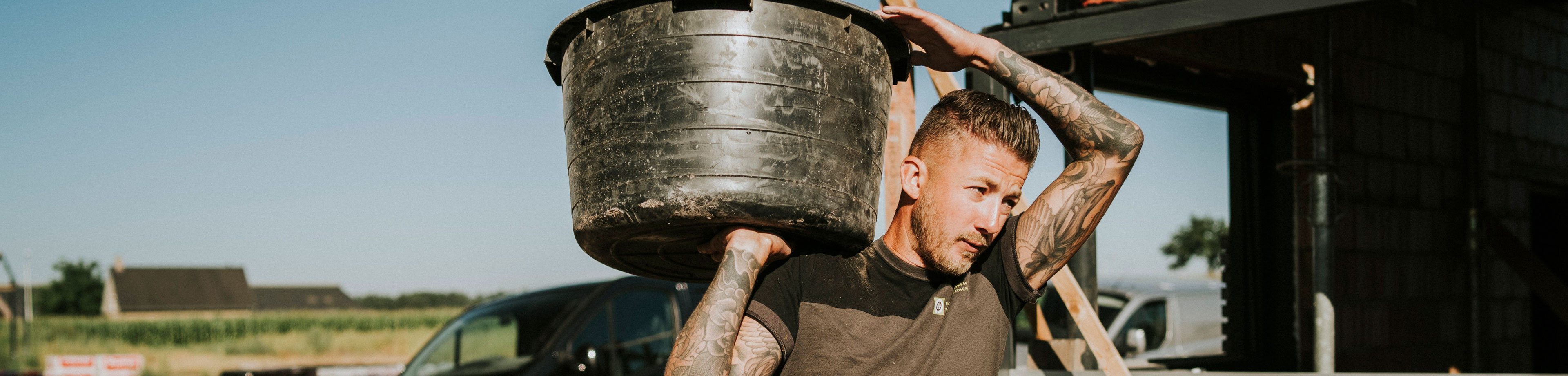 Een man in een donker t-shirt draagt tijdens het werken een speciekuip op zijn schouder.
