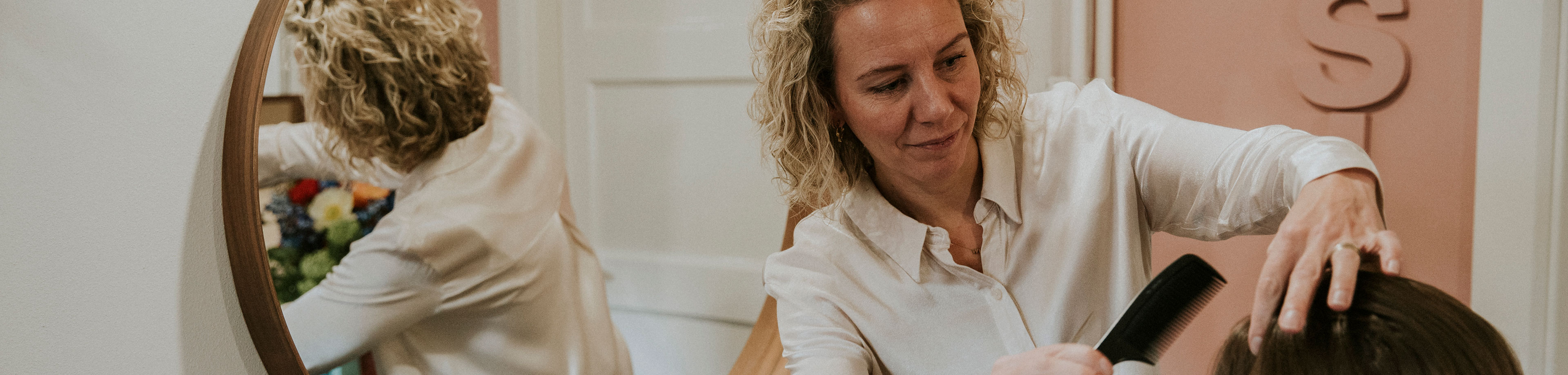 Een kapster met een witte blouse knipt het haar van een klant. Ze houdt een kam in haar handen.
