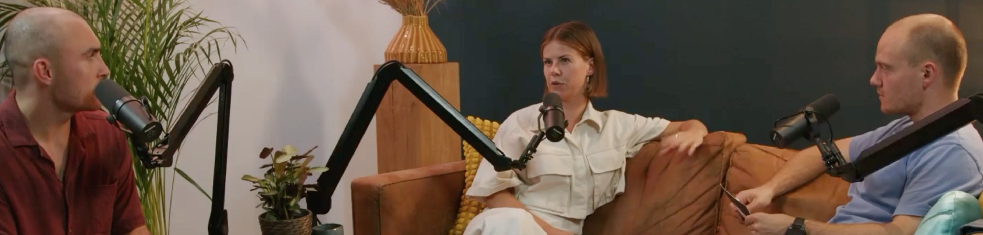 3 mensen zitten op een bank te praten met een microfoon voor zich