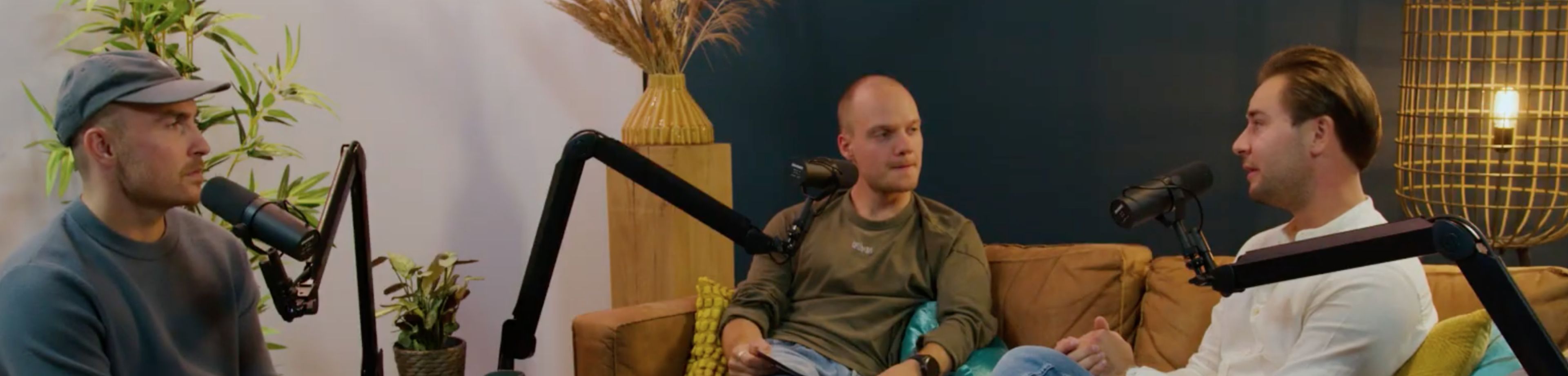 3 mensen zitten op een bank te praten, met een microfoon voor hun neus