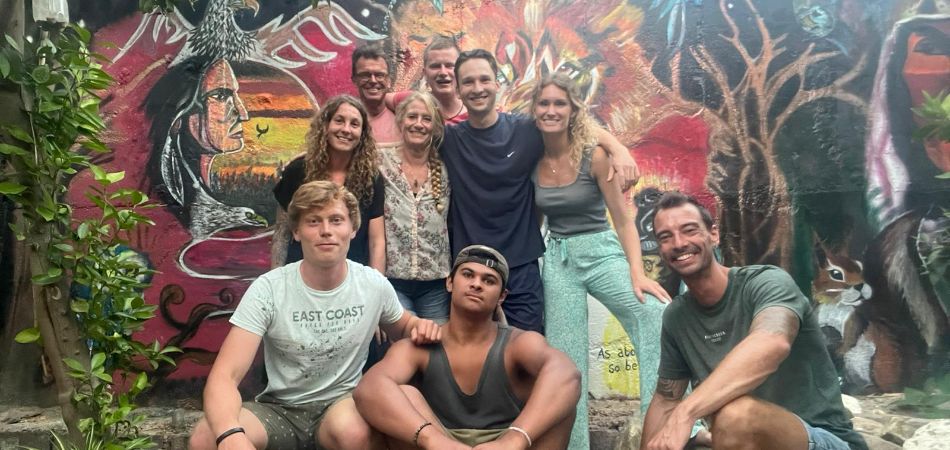 Een groep van 9 deelnemers aan het Route 66-programma, met op de achtergrond een kleurrijke muurschildering.