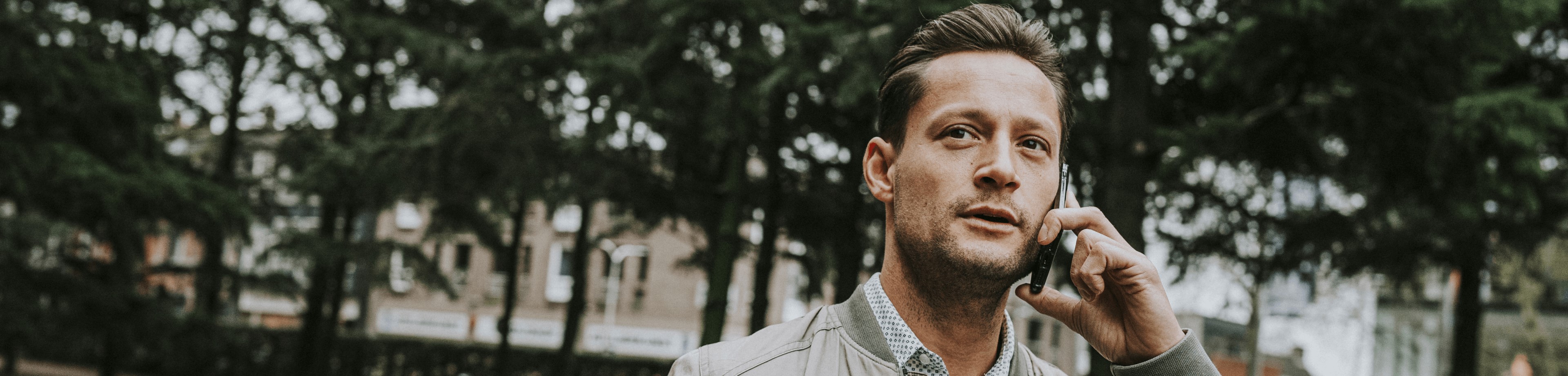 Een man loopt buiten in een park terwijl hij aan het bellen is