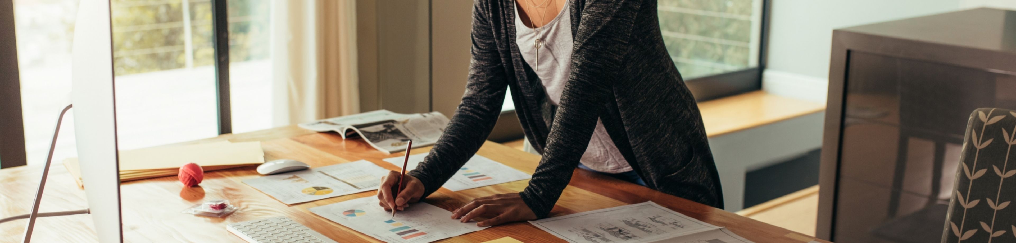 Een vrouw staat aan een bureau en schrijft iets op een stuk papier dat voor haar ligt.