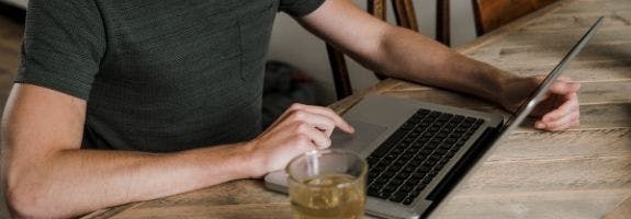 Man in t-shirt zit achter laptop, met een glas thee