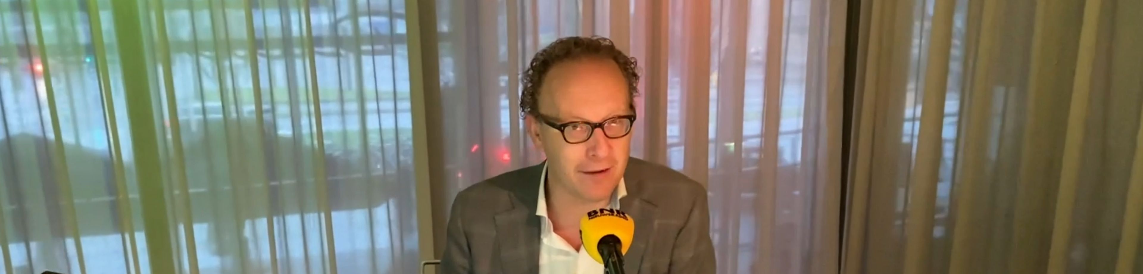 Man met bril zit aan een tafel achter een microfoon