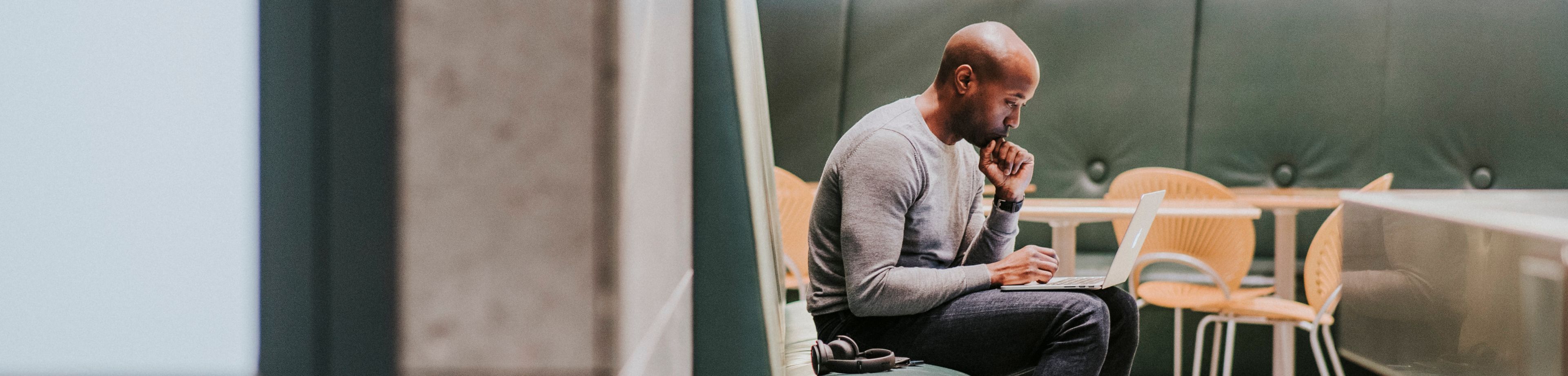 Man zit op een bank in een kantoor, met zijn laptop op schoot.