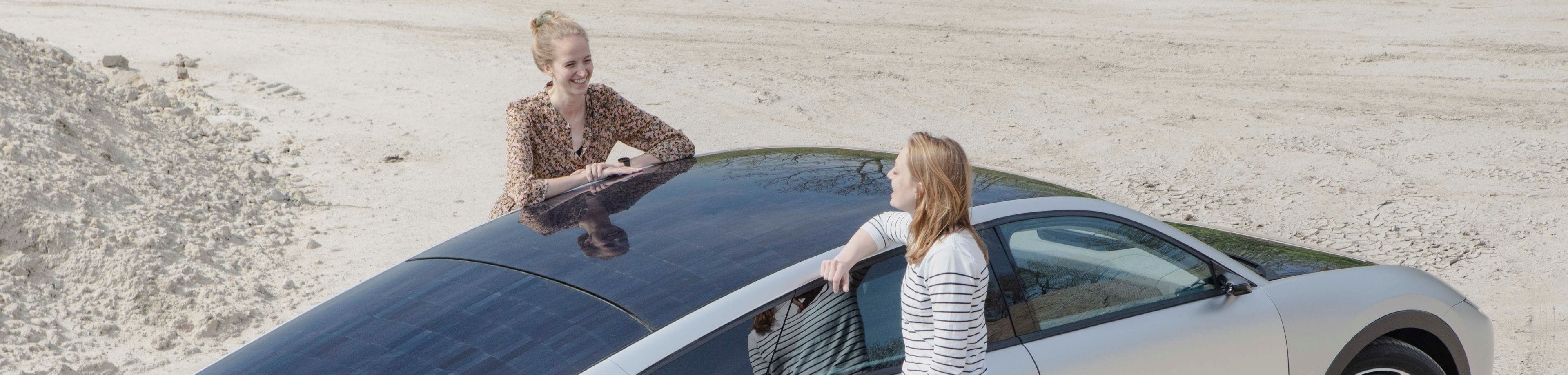 2 vrouwen praten met elkaar leunend op een auto op zonne-energie