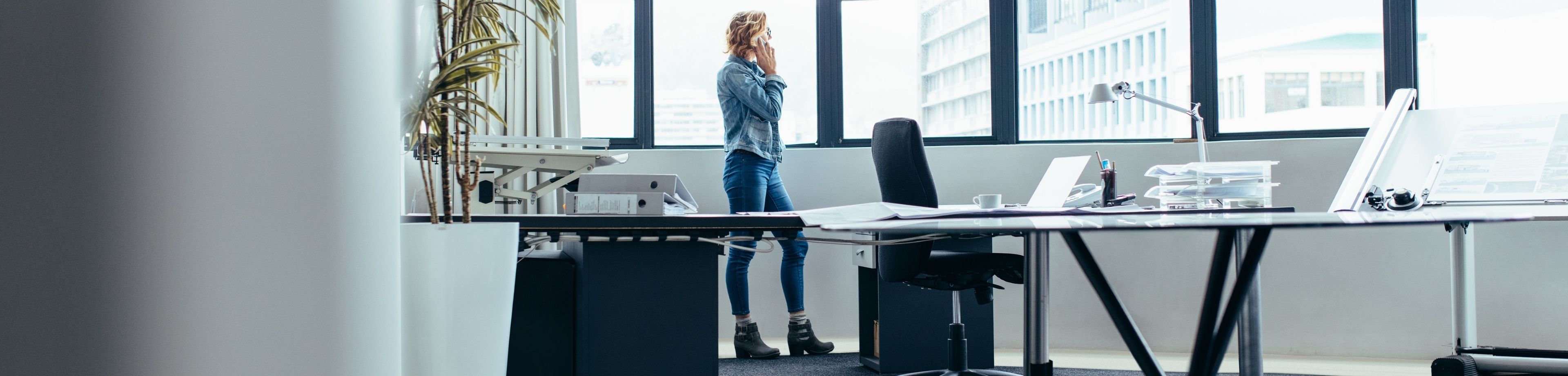 Vrouw staat bellend voor het raam in een kantoor