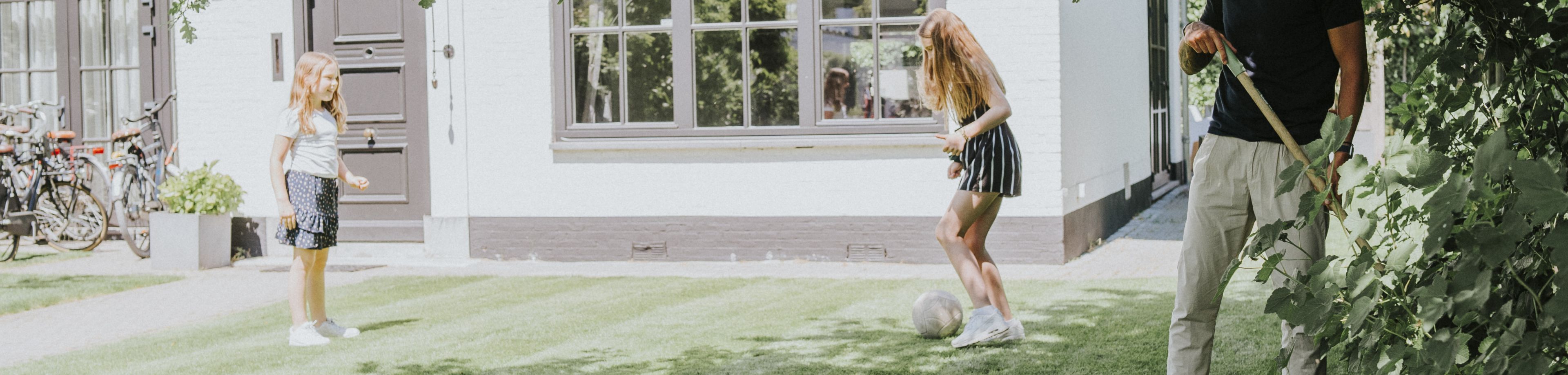 2 kinderen spelen op een zonnige dag in de tuin met een voetbal.