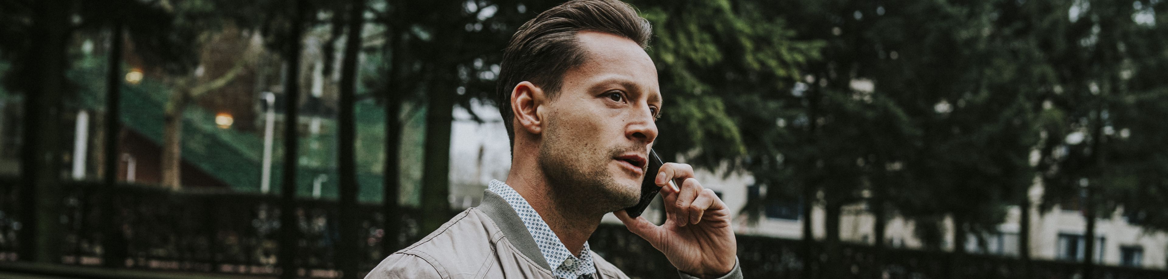 Een man staat met een telefoon aan zijn oor in een park