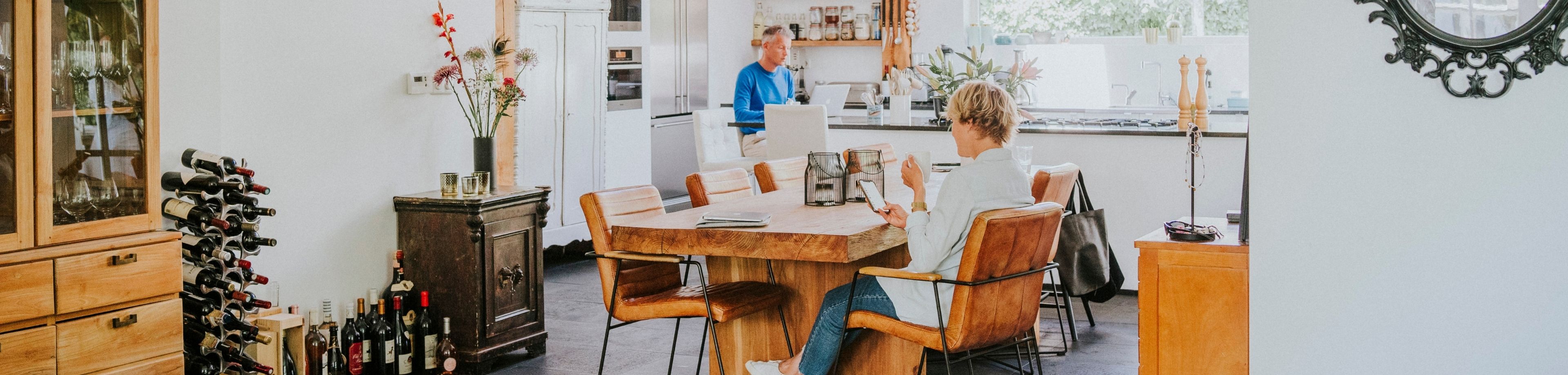 Vader en zoon aan het werk op de laptop in de keuken, zoon aan tafel en vader aan de bar
