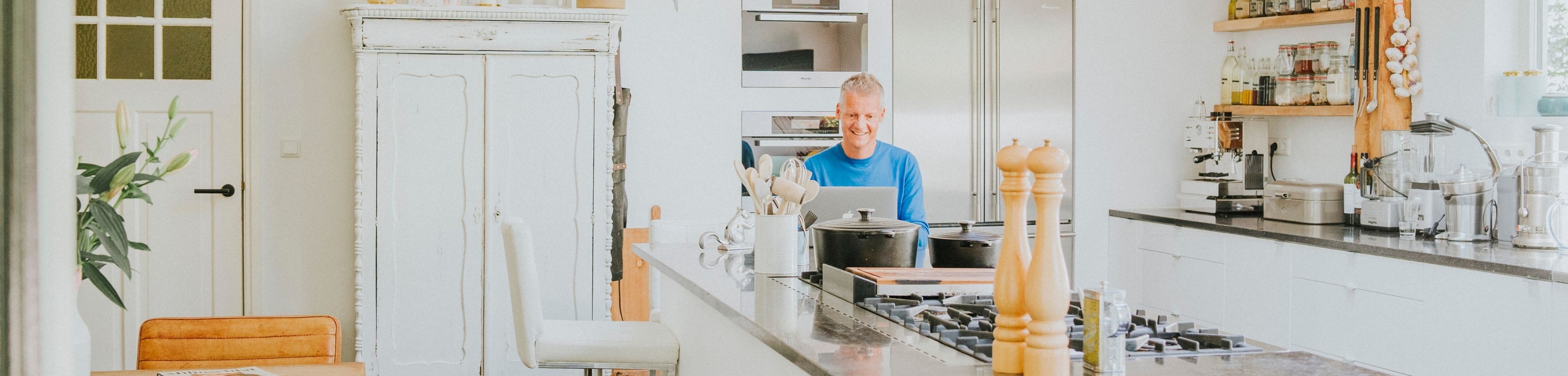 Vrolijke man zit achter laptop in een opgeruimde keuken