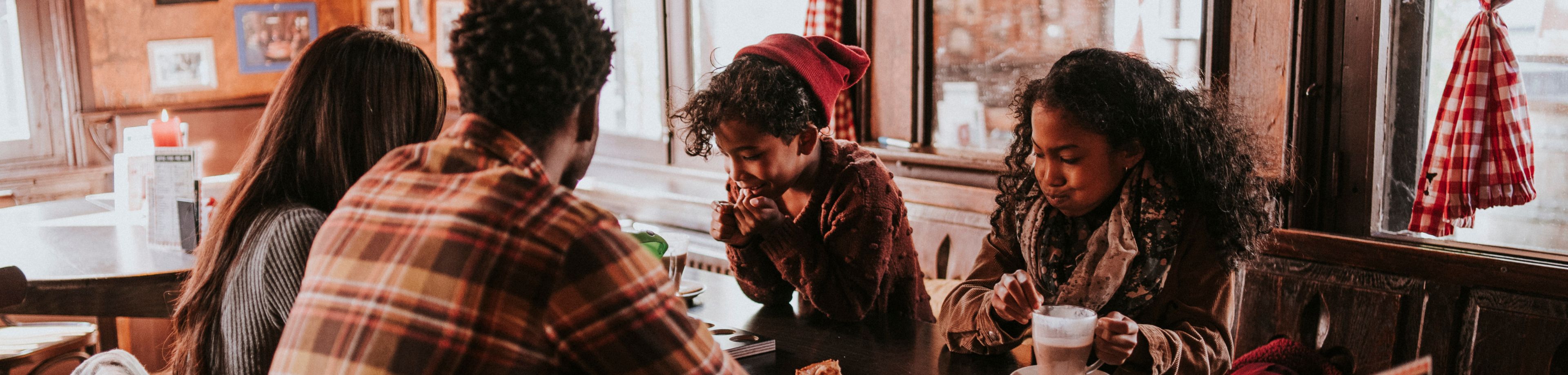 Een gezin zit in het najaar gezellig aan een tafeltje in een restaurant, te genieten van warme chocolademelk met slagroom.