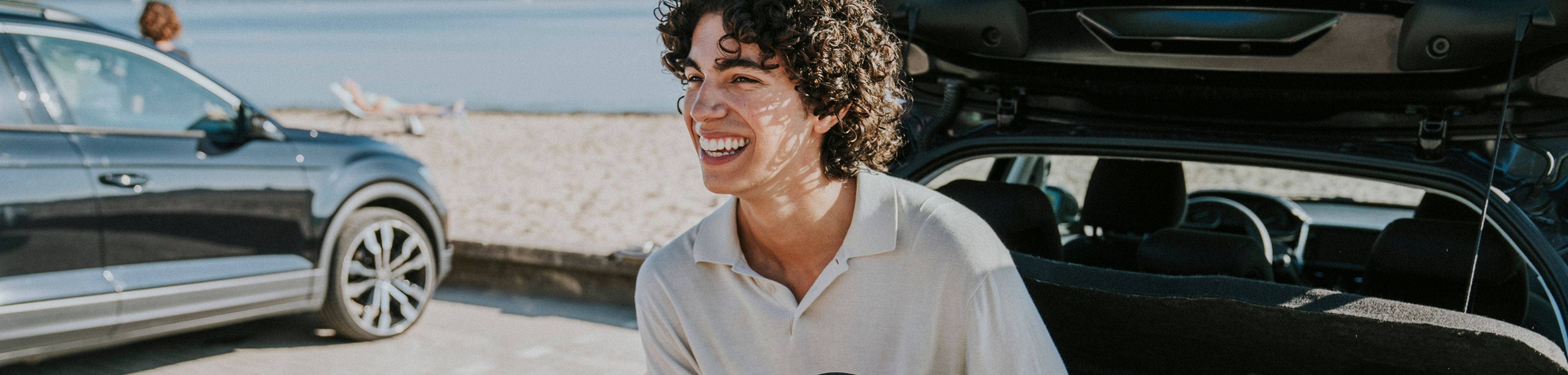 Een jonge man zit op de rand van de kofferbak van een auto en strikt zijn schoenveter