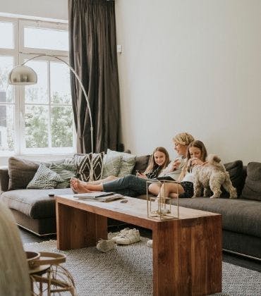 Een vrouw zit samen met 2 kinderen en een hond ontspannen op een bank in de woonkamer.