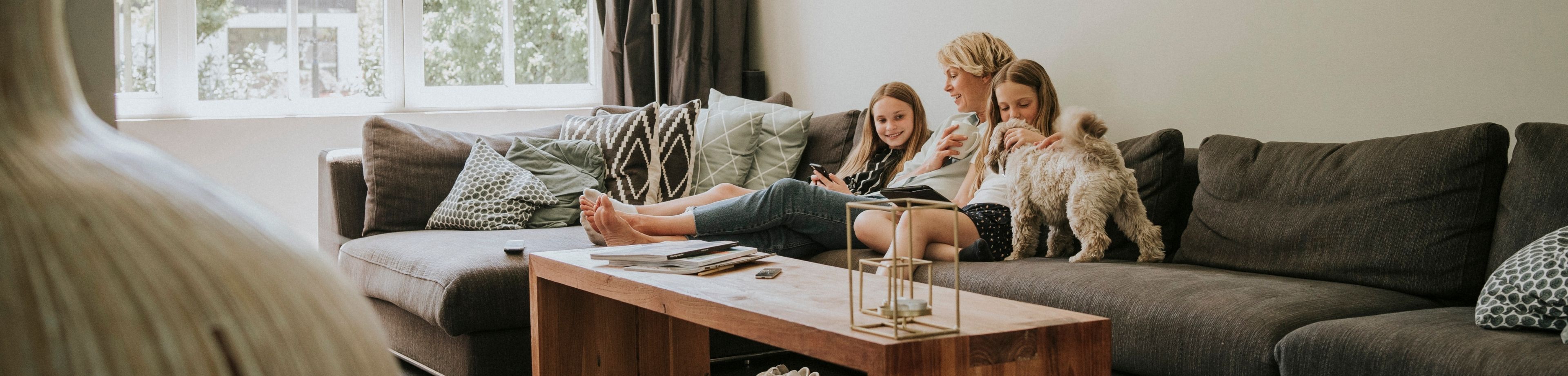 Een vrouw zit samen met 2 kinderen en een hond ontspannen op een bank in de woonkamer.