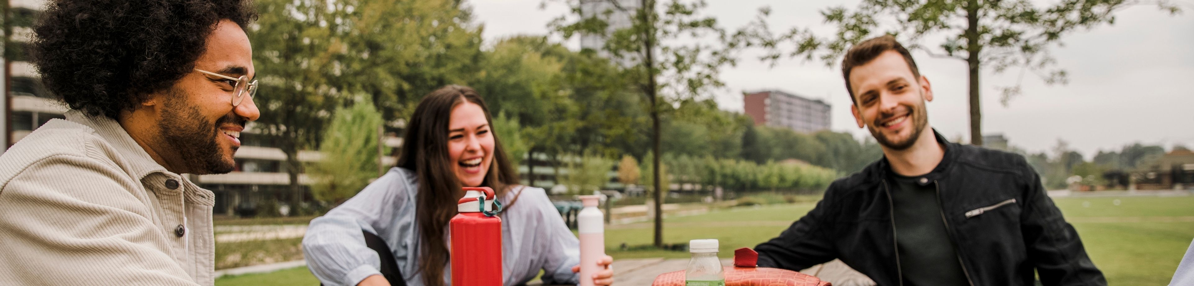 Een groepje jonge mensen zit bij elkaar aan een houten picknicktafel in een stadspark.