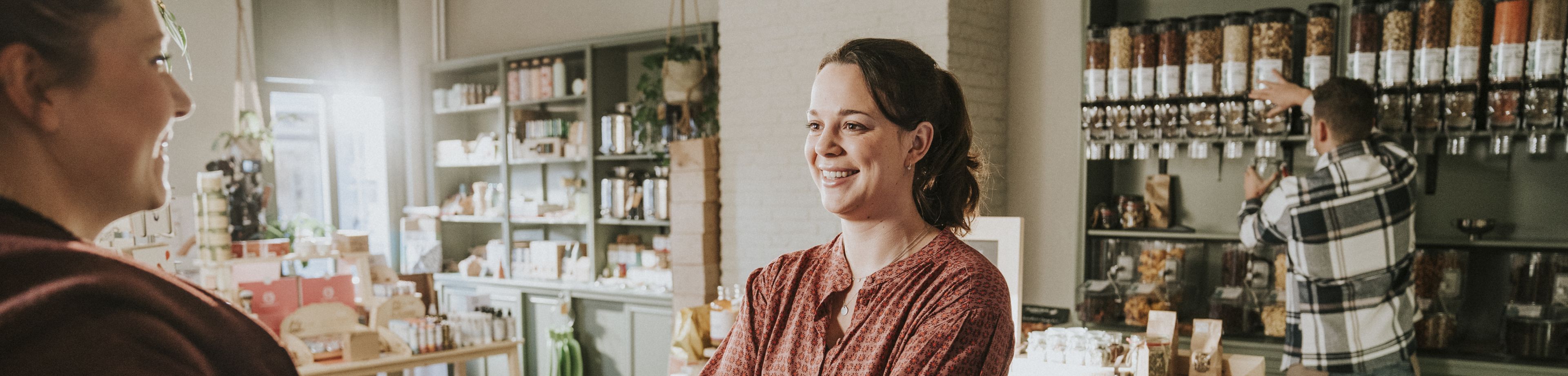 Een winkelier geeft een ingepakt doosje aan een klant, terwijl ze allebei vrolijk kijken.