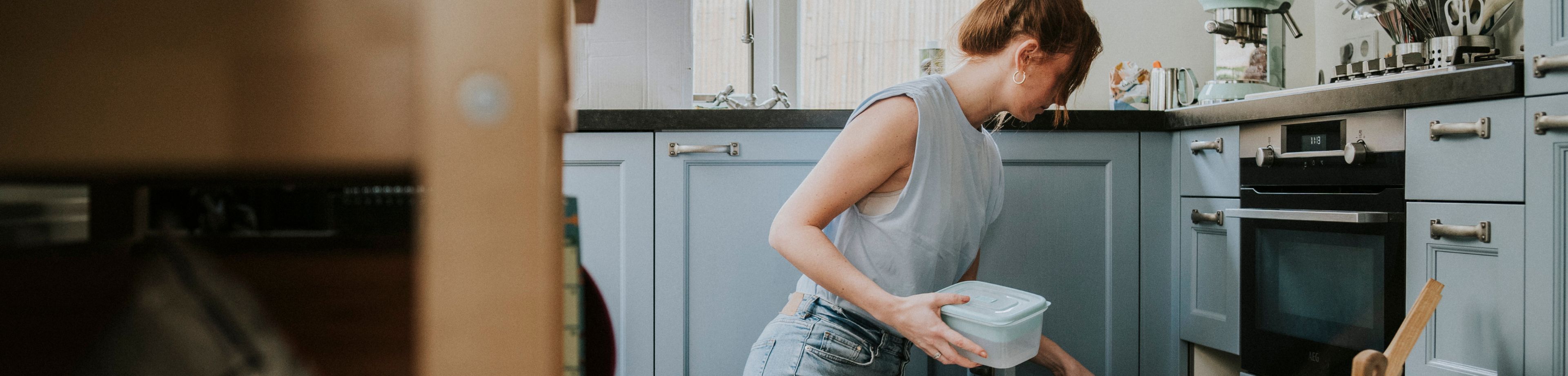 Een vrouw zit op haar knieën in de keuken bij verhuisdozen