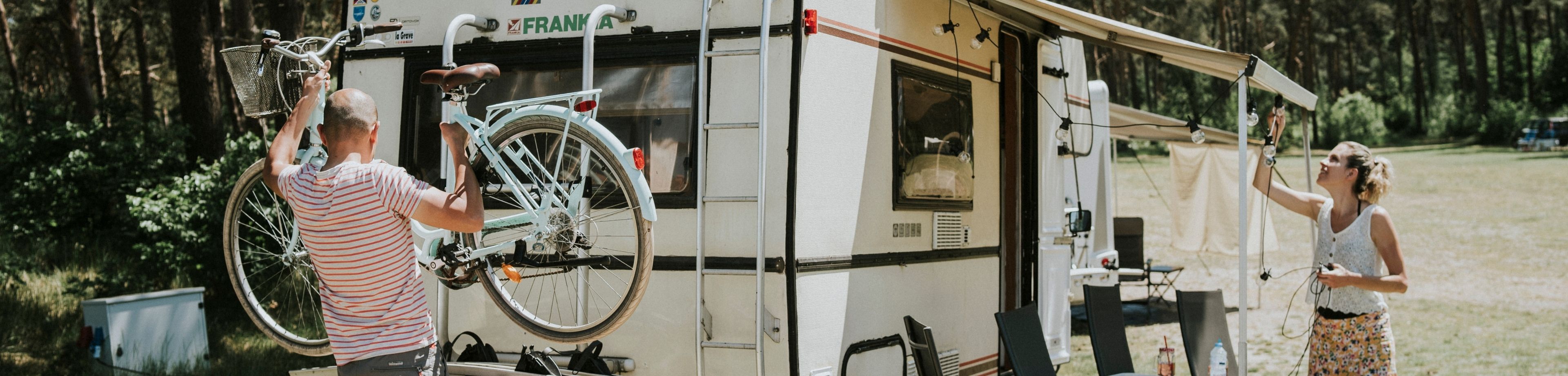 Man haalt fiets van de camper en vrouw hangt lampjes op aan het luifel van de camper.