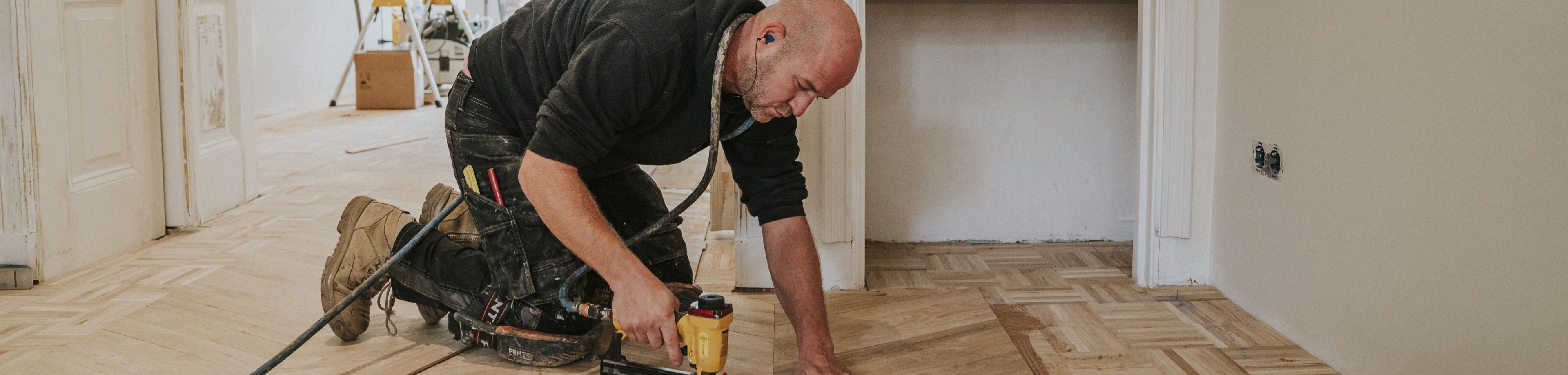 Een foto van man die op zijn knieën zit om een laminaat vloer te leggen.