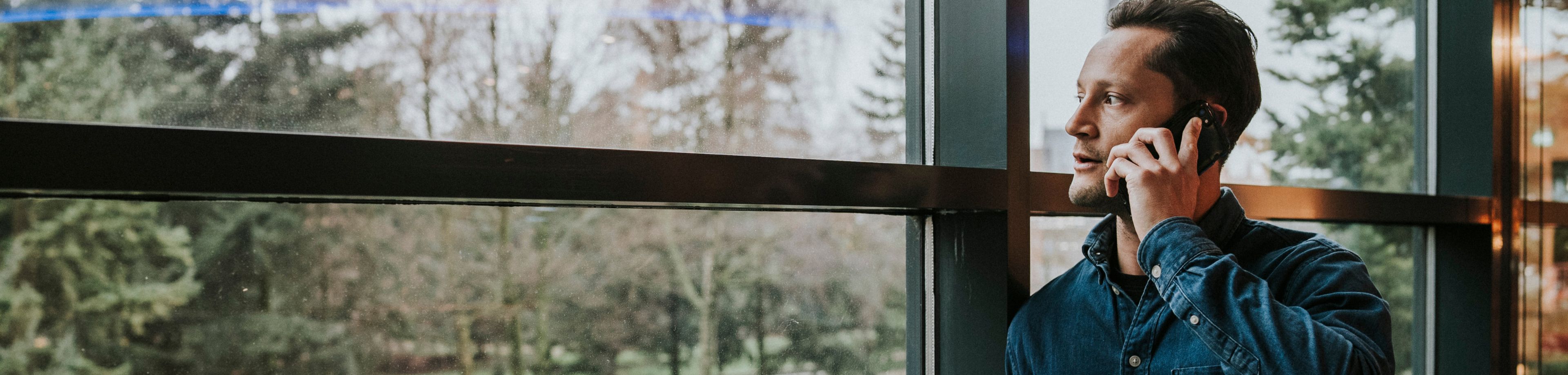 Een man staat te bellen bij het raam en kijkt naar buiten