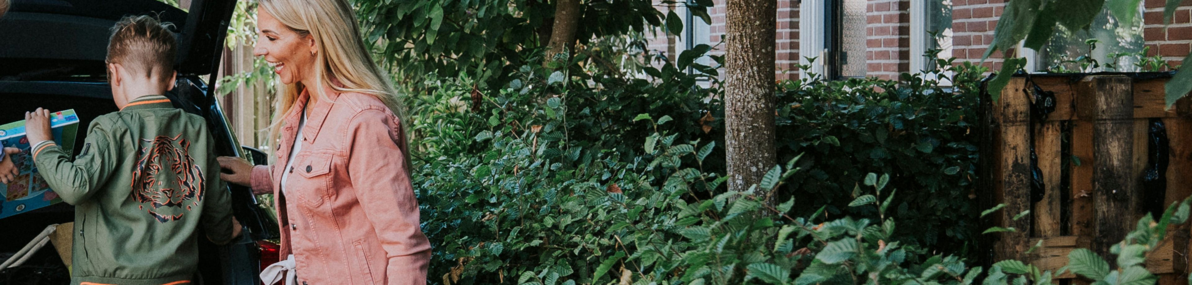 Vrouw staat bij auto met spullen achterin en kind zit op de rand van de kofferbak