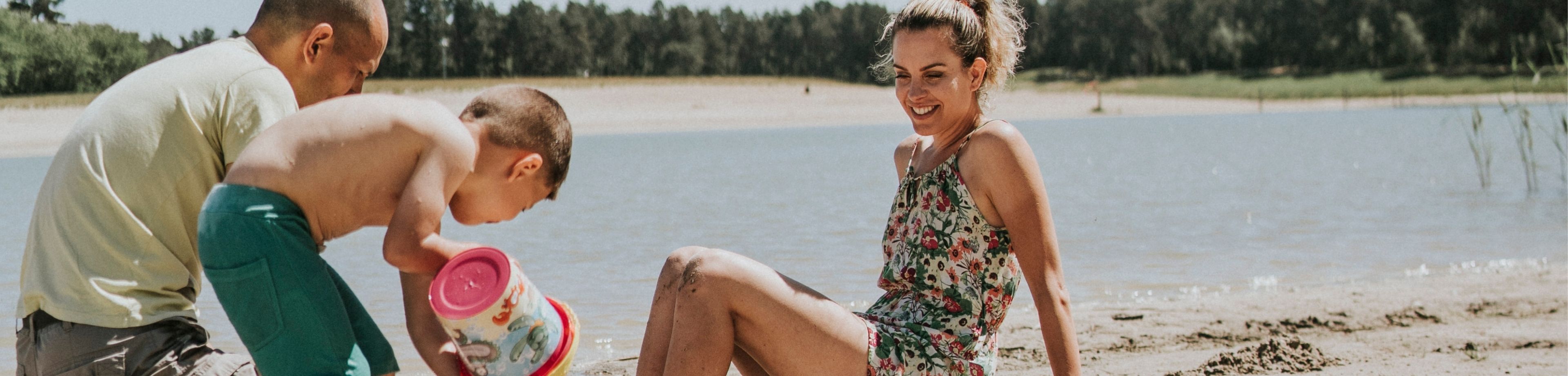Een zomerse dag; een gezin geniet op een strandje van de zon, en van het spelen met zand en water.
