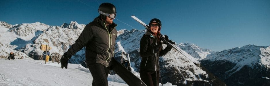 Man en vrouw lachend op de piste. Goed voorbereid op wintersport.