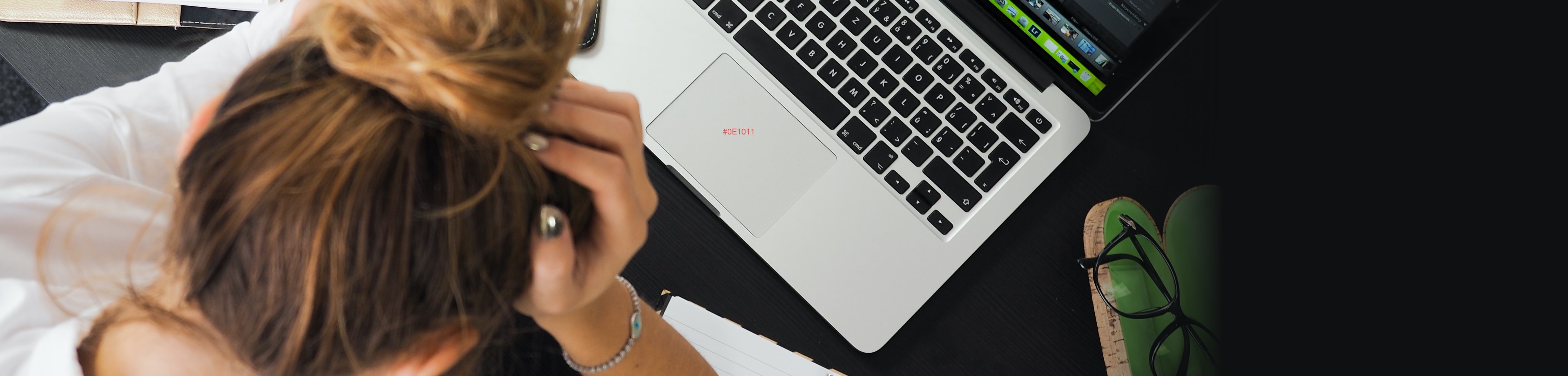 Vrouw die  voor haar laptop zit met haar hoofd in haar handen
