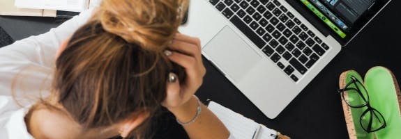 Vrouw die  voor haar laptop zit met haar hoofd in haar handen