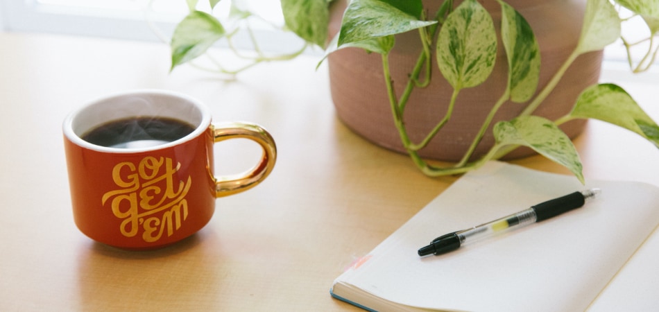 een tafel met daarop een kop koffie en een notitieblok met pen