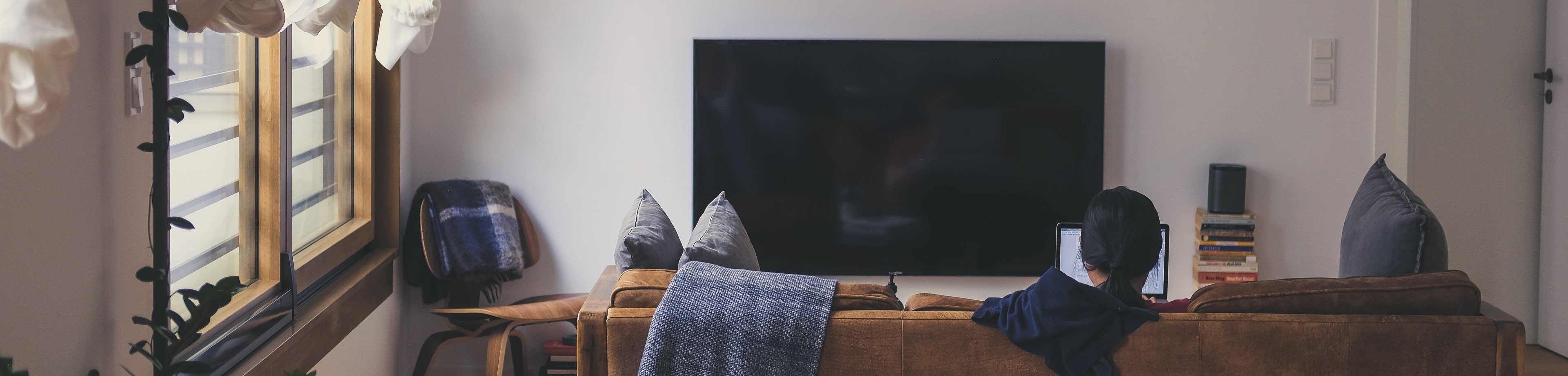 woonkamer met televisie en bank waarop iemand op zijn laptop werkt