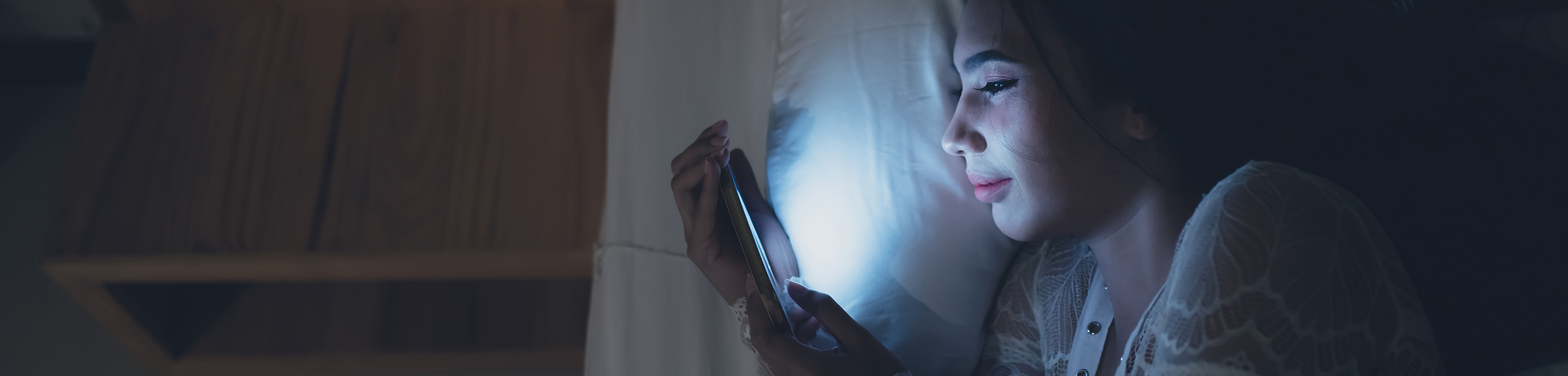 Meisje ligt in bed en kijkt op haar telefoon terwijl het verder donker is.